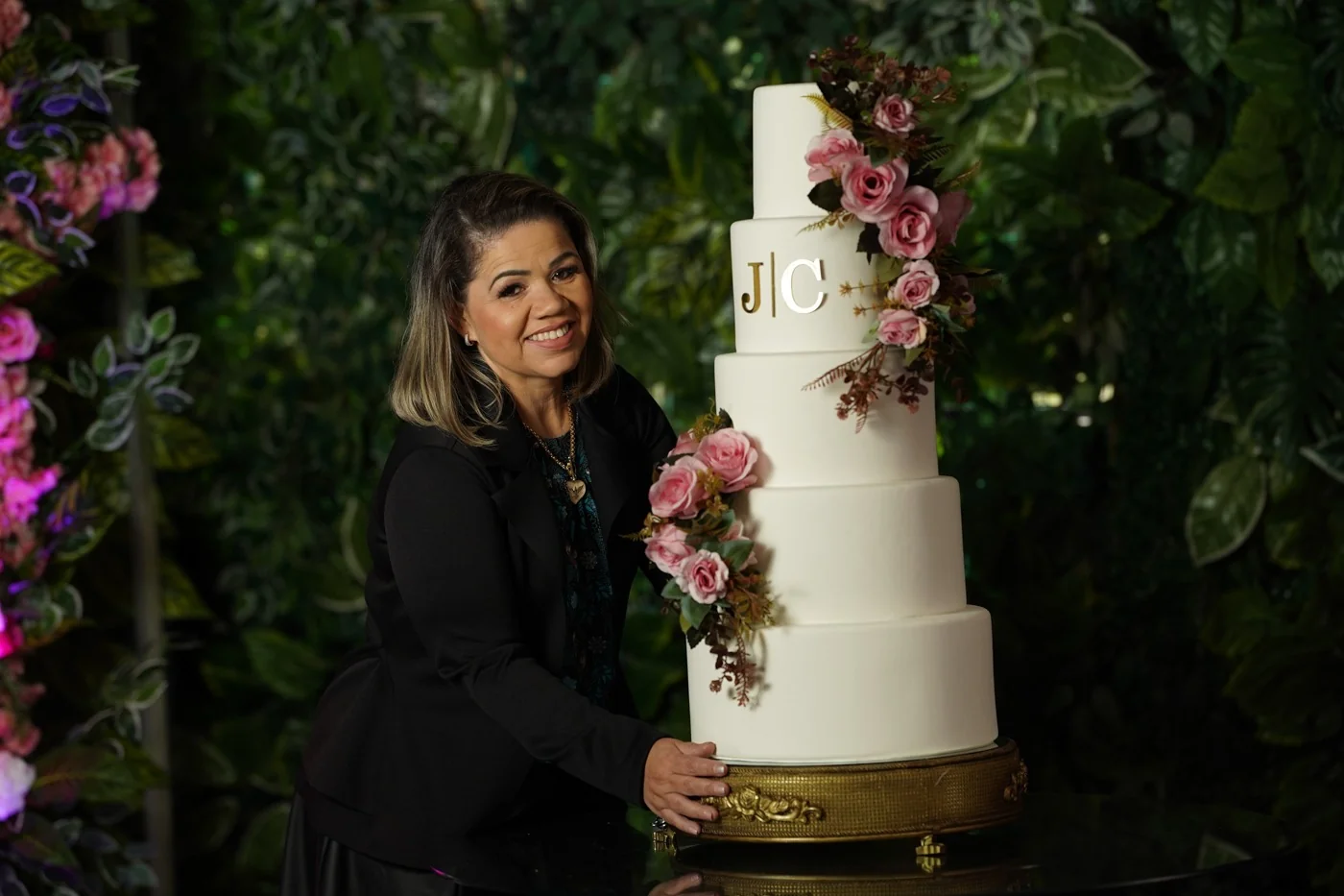 Eliane Cagé de roupa preta ao lado do bolo cenográfico com as iniciais JC