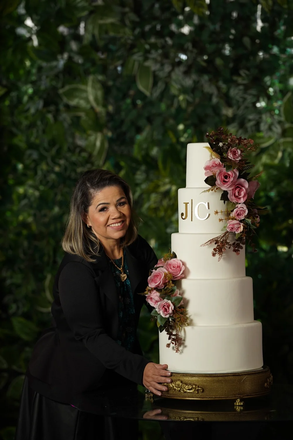 Eliane Cagé de roupa preta ao lado do bolo cenográfico com as iniciais JC